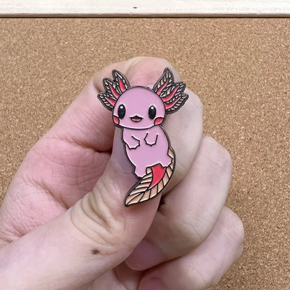 Pink axolotl enamel pin held between fingers against a beige background